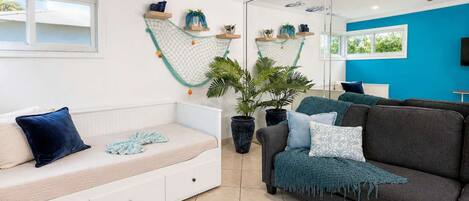 Un salon moderne avec un canapé blanc, un divan gris foncé et une grande plante en pot.