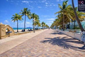 A beachfront promenade with palm trees, a beach, and a sign prohibiting glass containers.