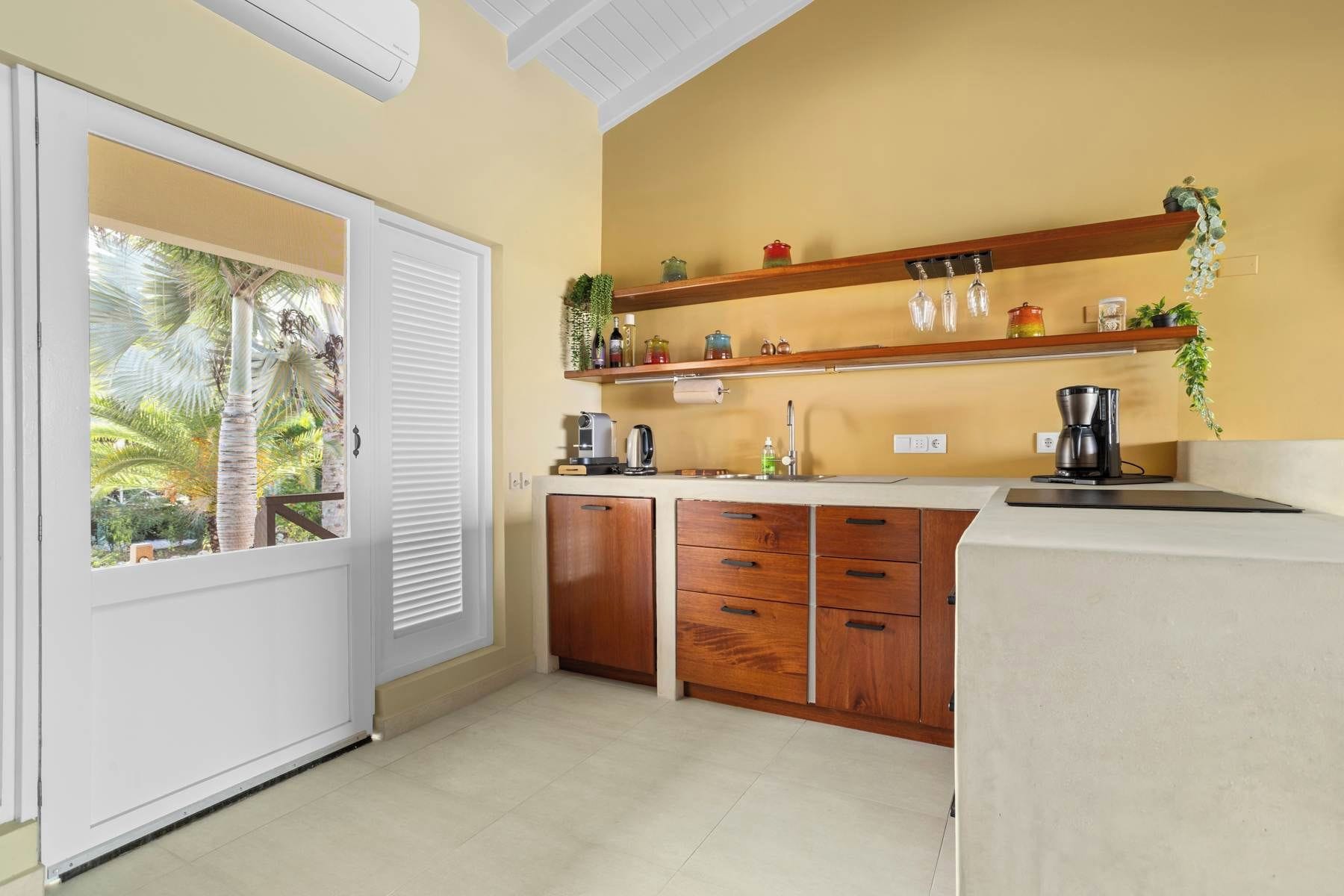 A compact kitchen with wooden cabinets, a coffee maker, and a window with a view of palm trees.