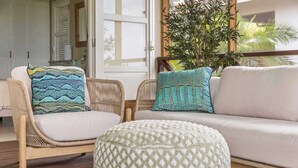 A living room with a wicker chair, a white sofa, and a patterned ottoman. - Villa Happy Turtle with a spectacular ocean view (Kralendijk)