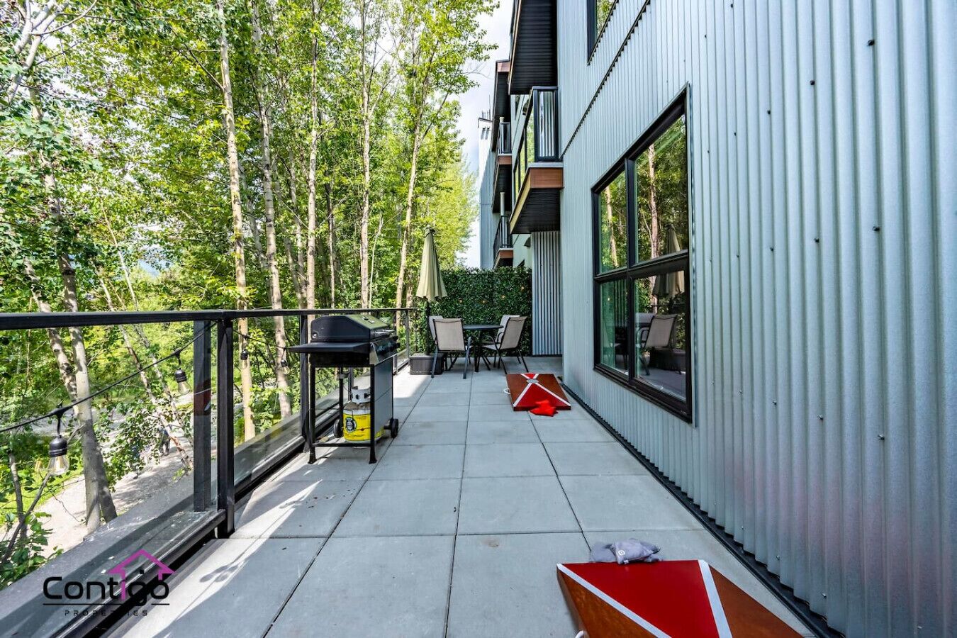 Un balcon doté d’un barbecue, de chaises et d’une table, le tout entouré d’arbres.