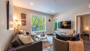 A modern living room with a sofa set, a coffee table, and a TV mounted on the wall. - Trailside Vista | Huge Patio | BBQ | AC | Downtown (Golden)