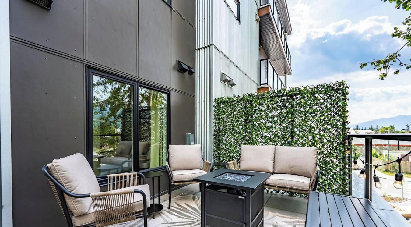 Une terrasse extérieure avec un canapé, des fauteuils et une table, entourée d’une haie et d’un mur de verre.
