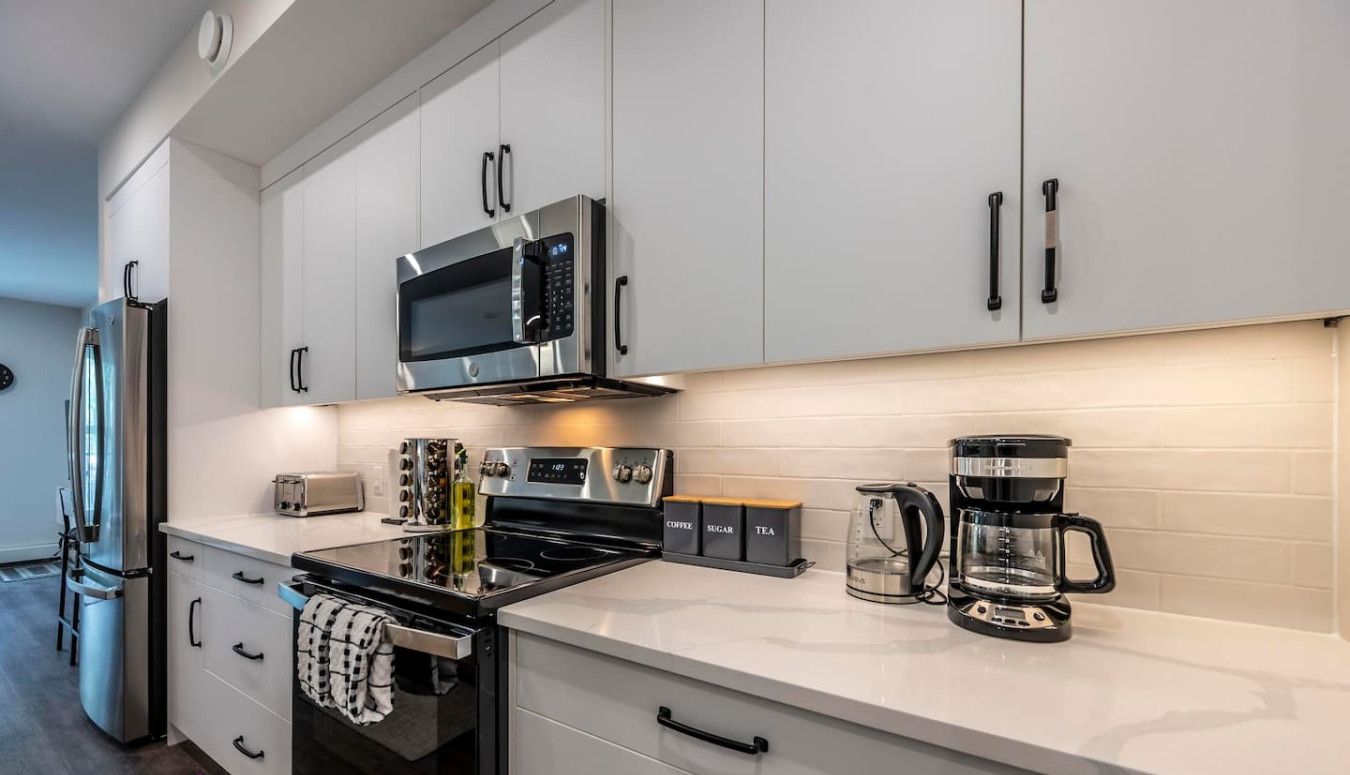 A modern kitchen with stainless steel appliances, white cabinetry, and a coffee maker.