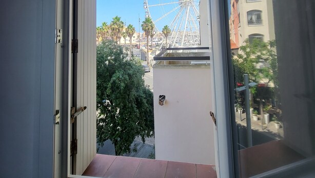 Vista per una finestra d'un edifici amb façana blanca, un balcó i un cel serè.