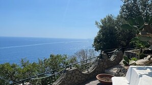 Une terrasse en pierre avec des meubles d’extérieur blancs, offrant une vue sur la côte.