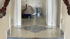 Un couloir doté d’un sol carrelé à motifs, un lit recouvert d’une couverture bleue et une petite table avec une lampe.
