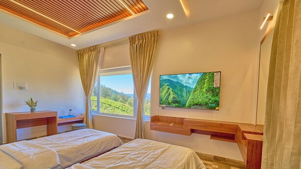 Een hotelkamer met twee bedden, een aan de muur bevestigde televisie, een houten bureau en een raam met uitzicht op groen.