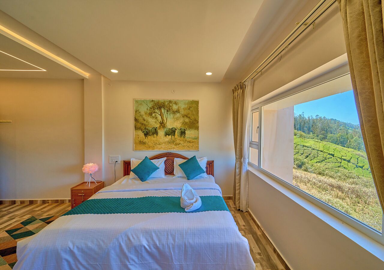 Een hotelkamer met een groot bed, een schilderij aan de muur en uitzicht op een groen landschap door het raam.