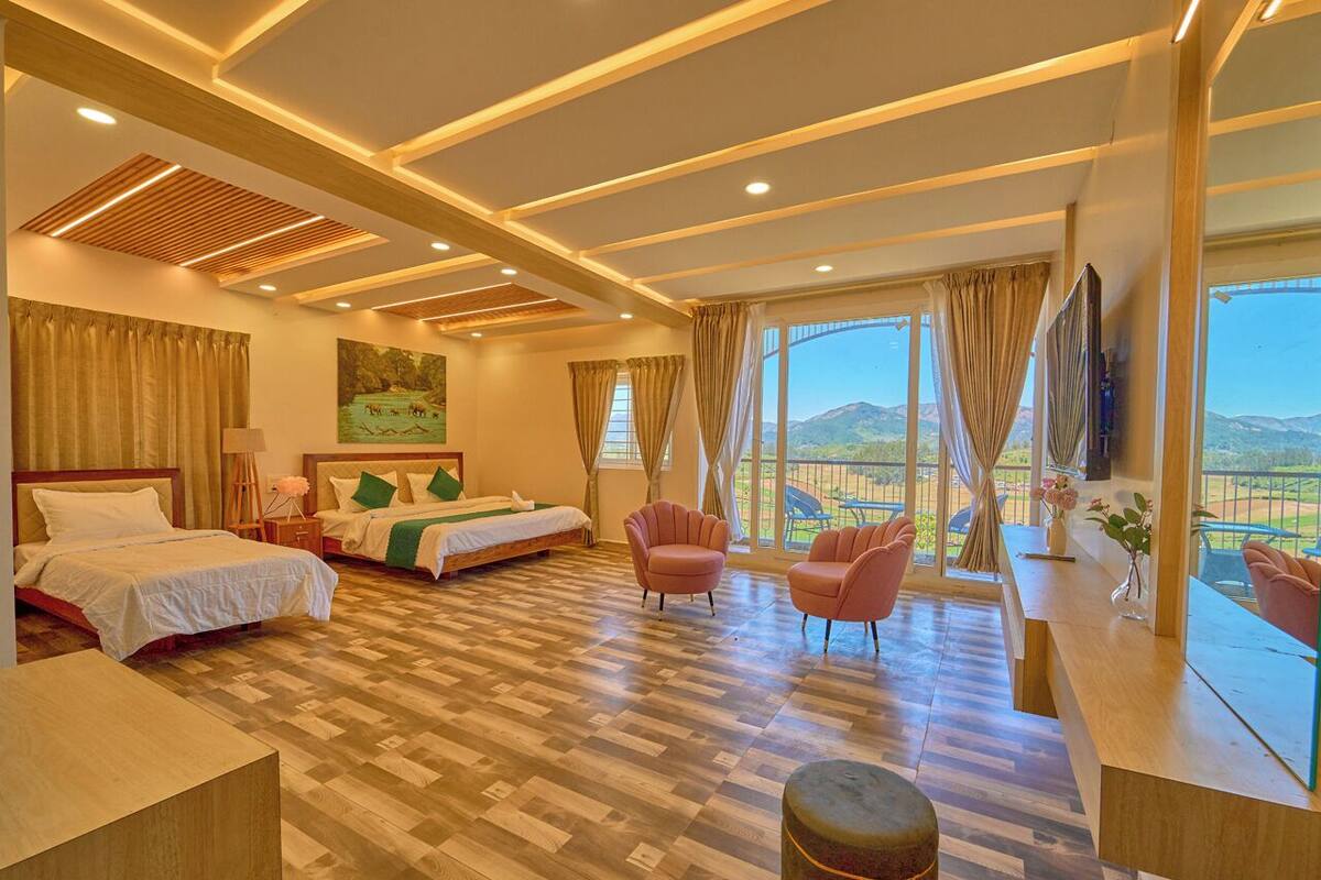 Habitación de hotel con una cama grande, dos camas más pequeñas, un escritorio y vistas a la montaña.