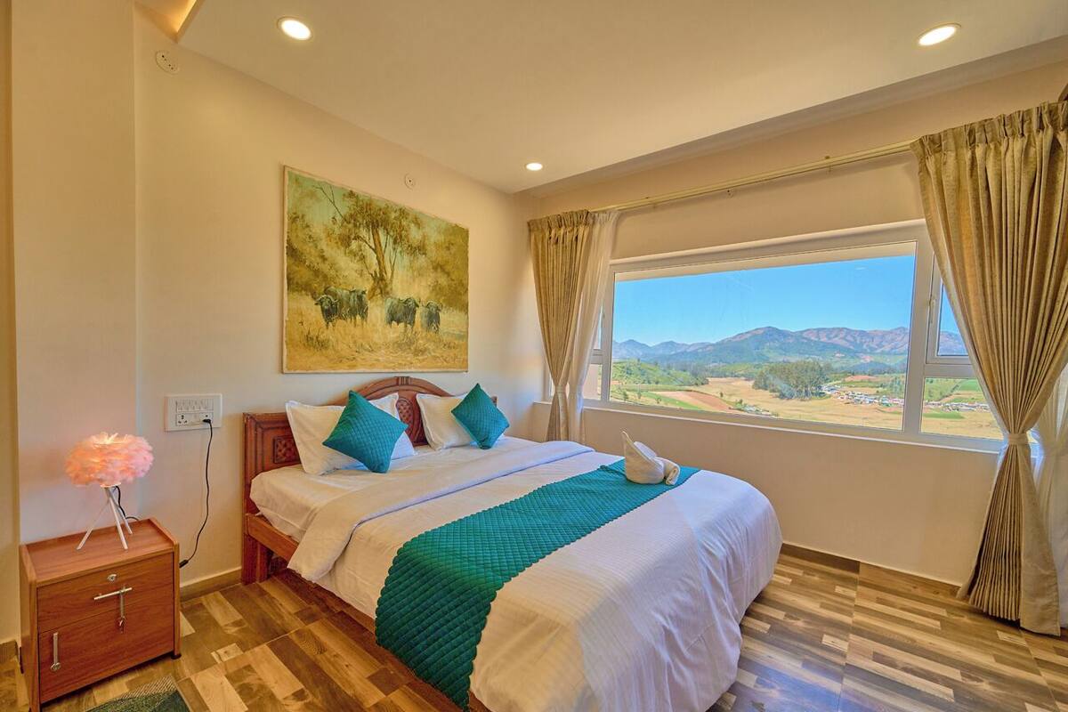 Un dormitorio con una cama grande, una mesita de noche, un cuadro y una ventana con vistas a las montañas.