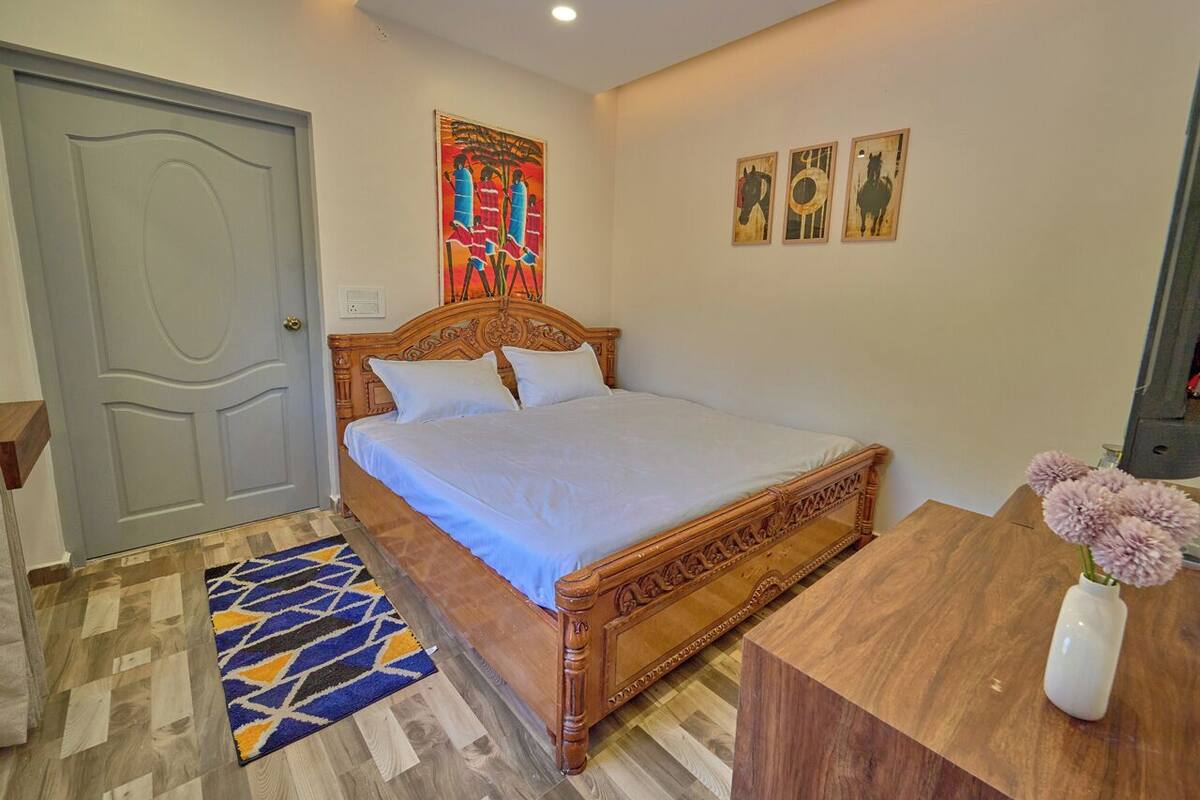 Un dormitorio con una cama de madera, un tapete estampado, una mesita de noche de madera y un florero con flores.