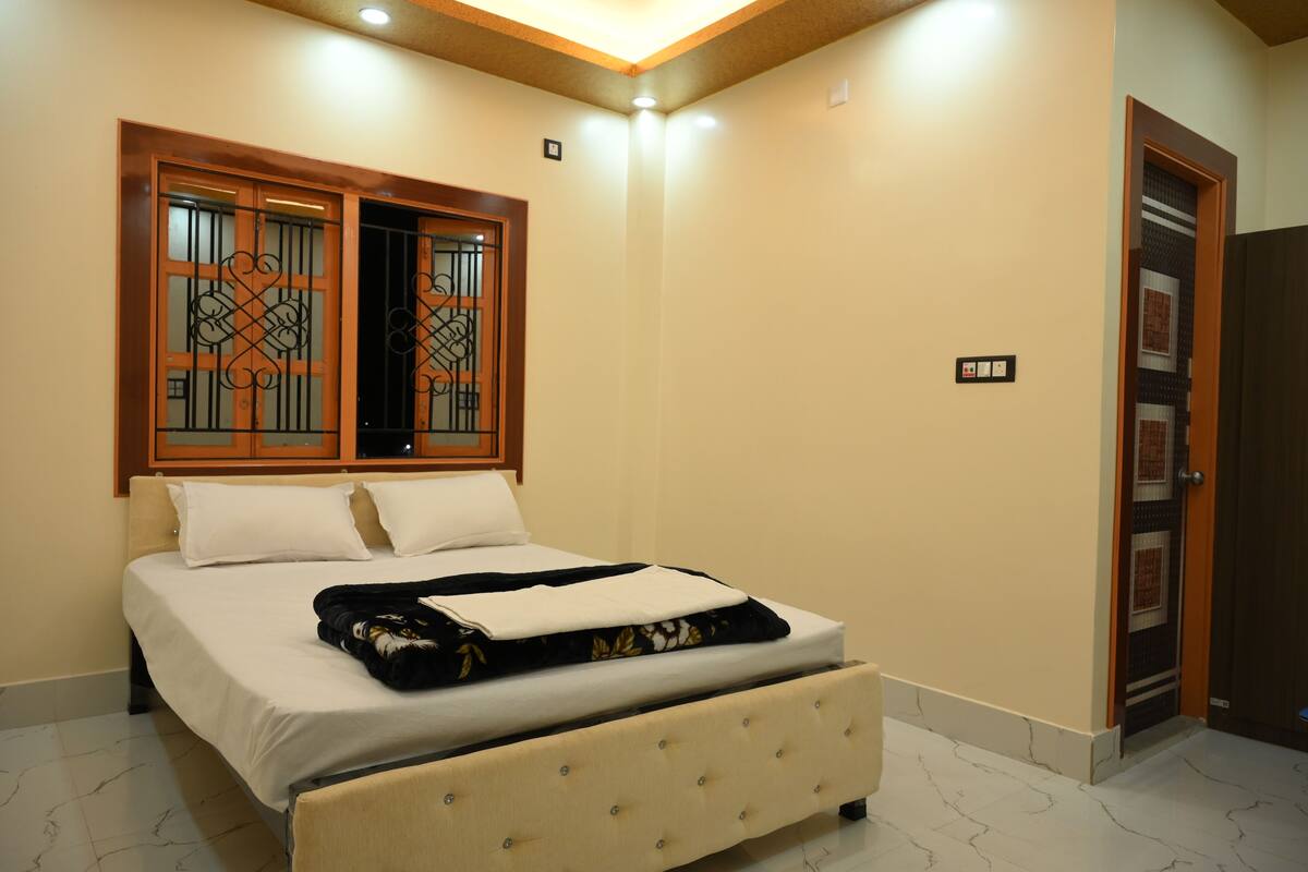 A bedroom with a bed, a window with decorative metal bars, a door, and a light switch on the wall.