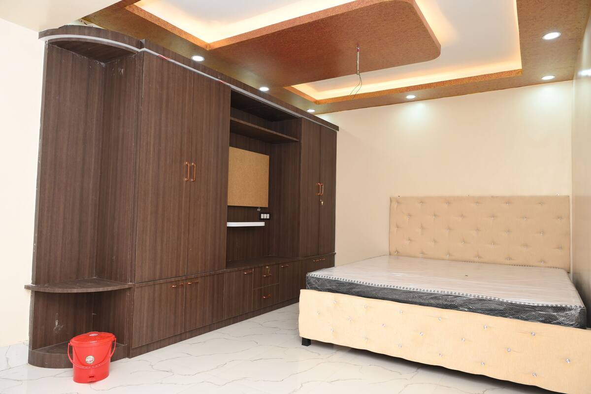 A bedroom with a bed, wardrobe, and a red bucket on the floor.