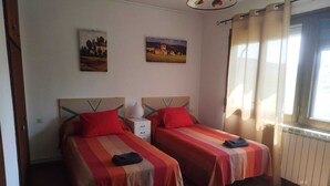 A room with two beds, each with a red and beige striped bedspread, a bedside table with a lamp, and two paintings on the wall.