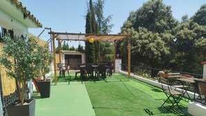 A patio with artificial grass, a pergola, outdoor furniture, and potted plants.