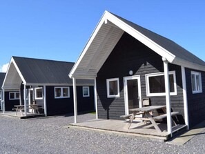 A row of small, dark-colored cabins with white trim, each featuring a porch and a picnic table. - 4 Star Holiday Home in Thyboron (Thyborøn)