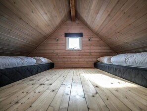 A small attic bedroom with wooden walls, a sloped ceiling, and a single window. There are two beds with mattresses and pillows. - 4 Star Holiday Home in Thyboron (Thyborøn)