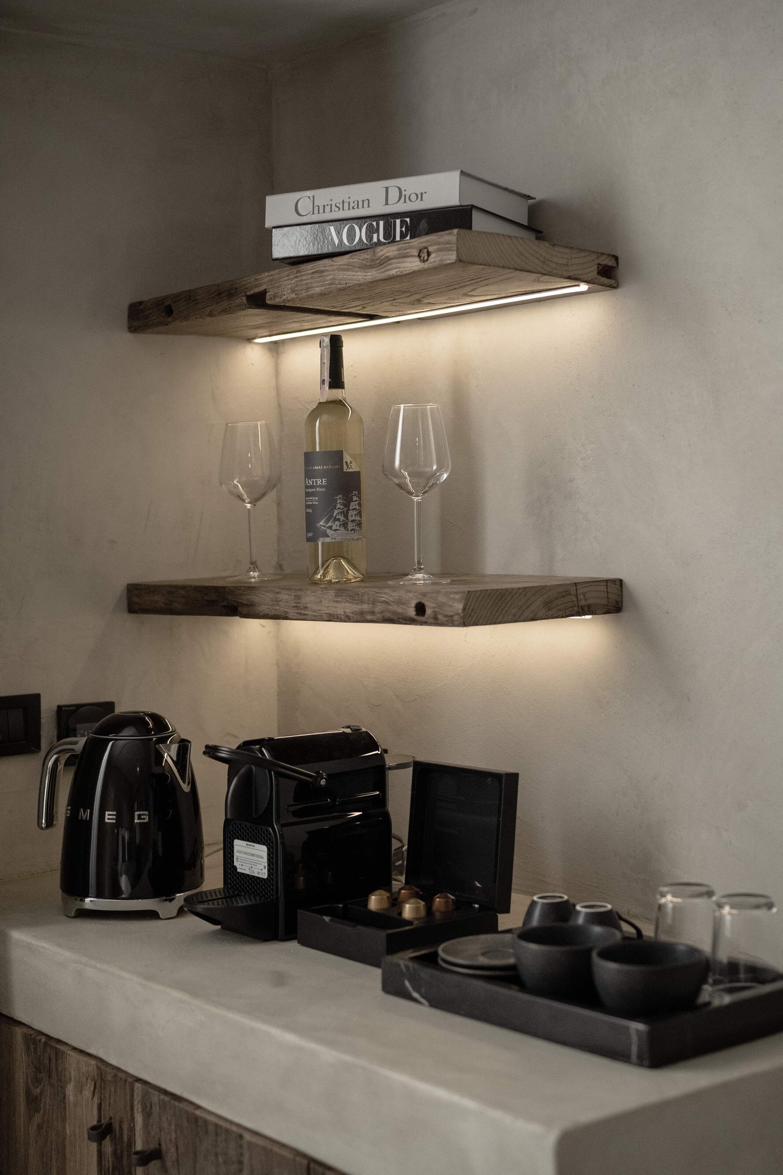 A kitchen counter with a coffee maker, a kettle, and a tray with cups and a bottle.