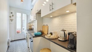 Une cuisine moderne avec des armoires blanches, un comptoir noir et un dosseret carrelé. On y trouve des tabourets près du comptoir et une machine à café sur la droite.