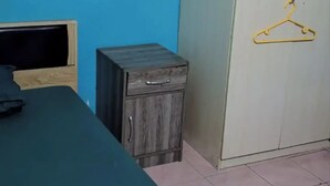 A room with a bed, a small wooden cabinet, and a wardrobe with a hanger.