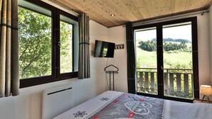 Une chambre dotée d’un grand lit, d’un téléviseur fixé au mur et d’un balcon offrant une vue sur la campagne.