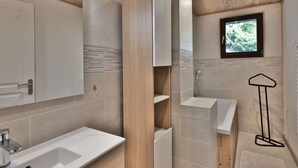 Une salle de bain moderne avec un plafond en bois, un grand miroir, un lavabo, une baignoire et une fenêtre donnant sur les arbres.