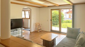 A spacious living room with a large TV, wooden furniture, and a sliding glass door leading to a garden. - Nice apartment for 6 people with WIFI, TV, terrace and pets allowed (Reutte)