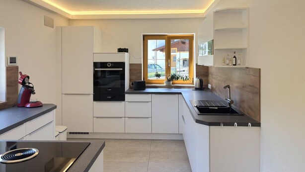 A modern kitchen with white cabinets, a built-in oven, a sink, and a window with a view of the outside. - Nice apartment for 6 people with WIFI, TV, terrace and pets allowed (Reutte)
