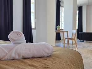 A neatly made bed with a rolled towel, a wooden chair, and a small table with a plant in a hotel room. - Design suites in central Malaga, near museums and Calle Larios (Málaga)