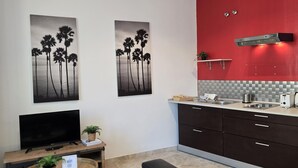 A modern kitchen with a red accent wall, two black and white palm tree paintings, a flat-screen TV, a small table with a plant, and a black chair. - Design suites in central Malaga, near museums and Calle Larios (Málaga)