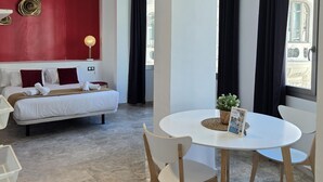 A hotel room with a bed, a small table with chairs, a red accent wall, and a window with curtains. - Design suites in central Malaga, near museums and Calle Larios (Málaga)