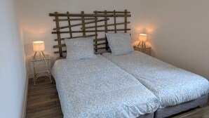 Een tweepersoonsbed met een houten hoofdbord, twee bedlampjes en een beddegoed met een patroon.