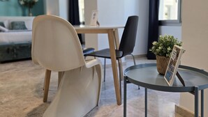 A modern living room with a sofa, a dining table, and chairs. There is a small round table with a plant and a framed picture. - Félix Sáenz Suites: Design Accommodation in Malaga Center (Málaga)