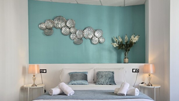 A modern bedroom with a large bed, two bedside tables with lamps, a decorative wall piece, and a vase with flowers. - Félix Sáenz Suites: Design Accommodation in Malaga Center (Málaga)