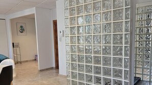 A hallway with a glass partition wall, a door, and a small table with a trash bin. - Félix Sáenz Suites: Design Accommodation in Malaga Center (Málaga)
