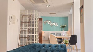 A room with a blue upholstered sofa, a wooden ladder, a teal wall, a dining area with a table and chairs, and a small plant. - Félix Sáenz Suites: Design Accommodation in Malaga Center (Málaga)