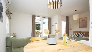 A cozy living area with a round wooden table, a green sofa, and a dining table set with wine glasses and a bottle.