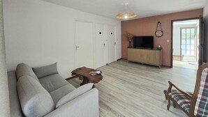 Una sala de estar con un sofá, una mesa de centro de madera, un televisor sobre un mueble y una puerta.