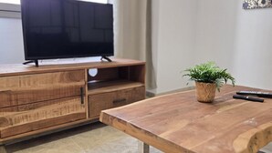 A wooden TV stand with a flat-screen TV, a potted plant, and two remote controls on a wooden table. - Design Suites in Malaga Center - Comfortable Accommodation (Málaga)