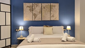 A hotel room with a large bed, two bedside lamps, a world map artwork above the bed, and a small round table with a lamp. - Design Suites in Malaga Center - Comfortable Accommodation (Málaga)