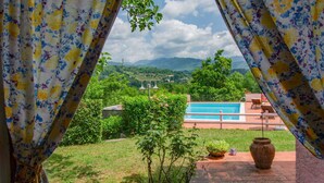 Vista attraverso tende di una piscina, vegetazione e montagne lontane.