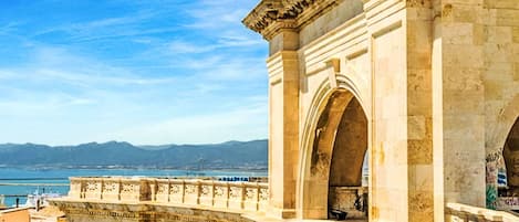 A historic stone bridge with arches and intricate carvings, overlooking a body of water and distant mountains.