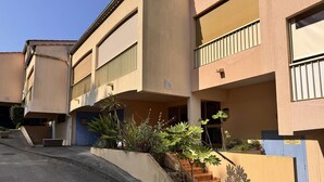A multi-story building with a flat facade, a blue door, and a small garden area with plants and a staircase.