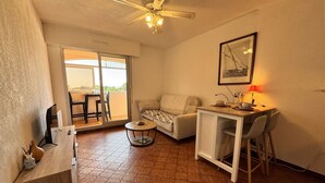Un salon confortable avec un canapé, une petite table, un ventilateur de plafond et un balcon équipé de chaises.