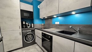 Una cocina moderna con armarios grises, lavadora, lavavajillas y un lavabo con grifo.