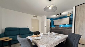 Un comedor moderno con una mesa preparada para cuatro personas, un sofá color turquesa y una cocina al fondo.