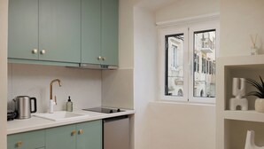 Une cuisine avec des armoires de couleur turquoise, un évier blanc et une fenêtre donnant sur des immeubles.