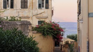 Une rue étroite bordée de vieux bâtiments, une moto et une vue sur la mer.