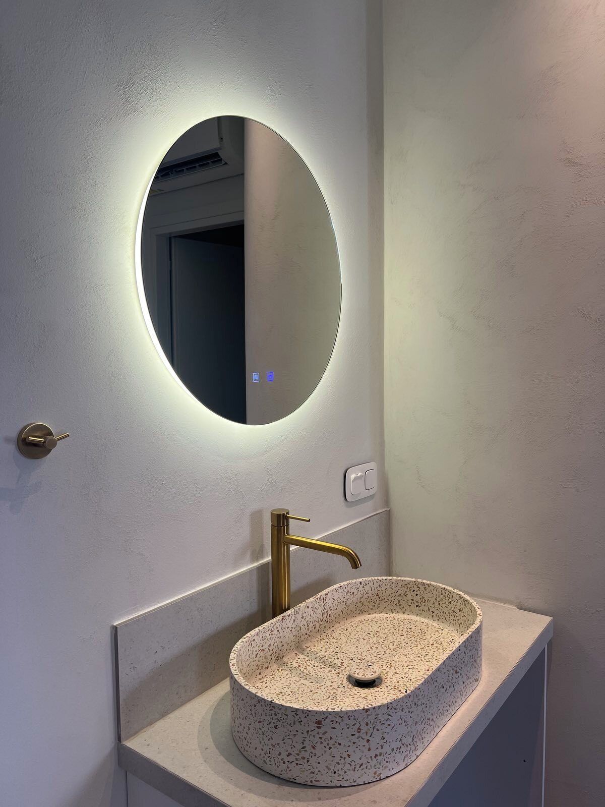 Ein Badezimmer mit einem runden Spiegel, einem goldenen Wasserhahn und einem Waschbecken mit Farbspeckeln.